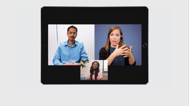 A tablet device screen shows a video call with three people on it. To the left is a man wearing a blue button-down top with a white background. To the right is an interpreter, signing in ASL. At the bottom is a woman with long black hair, sitting on a couch, wearing a pink tee.